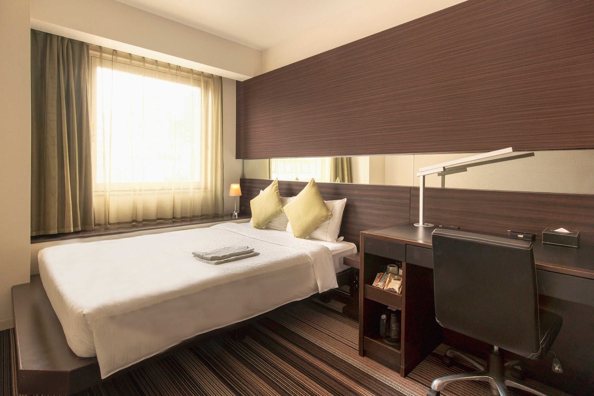 Een hotelkamer met een groot bed, een bureau, een stoel en een raam met gordijnen.