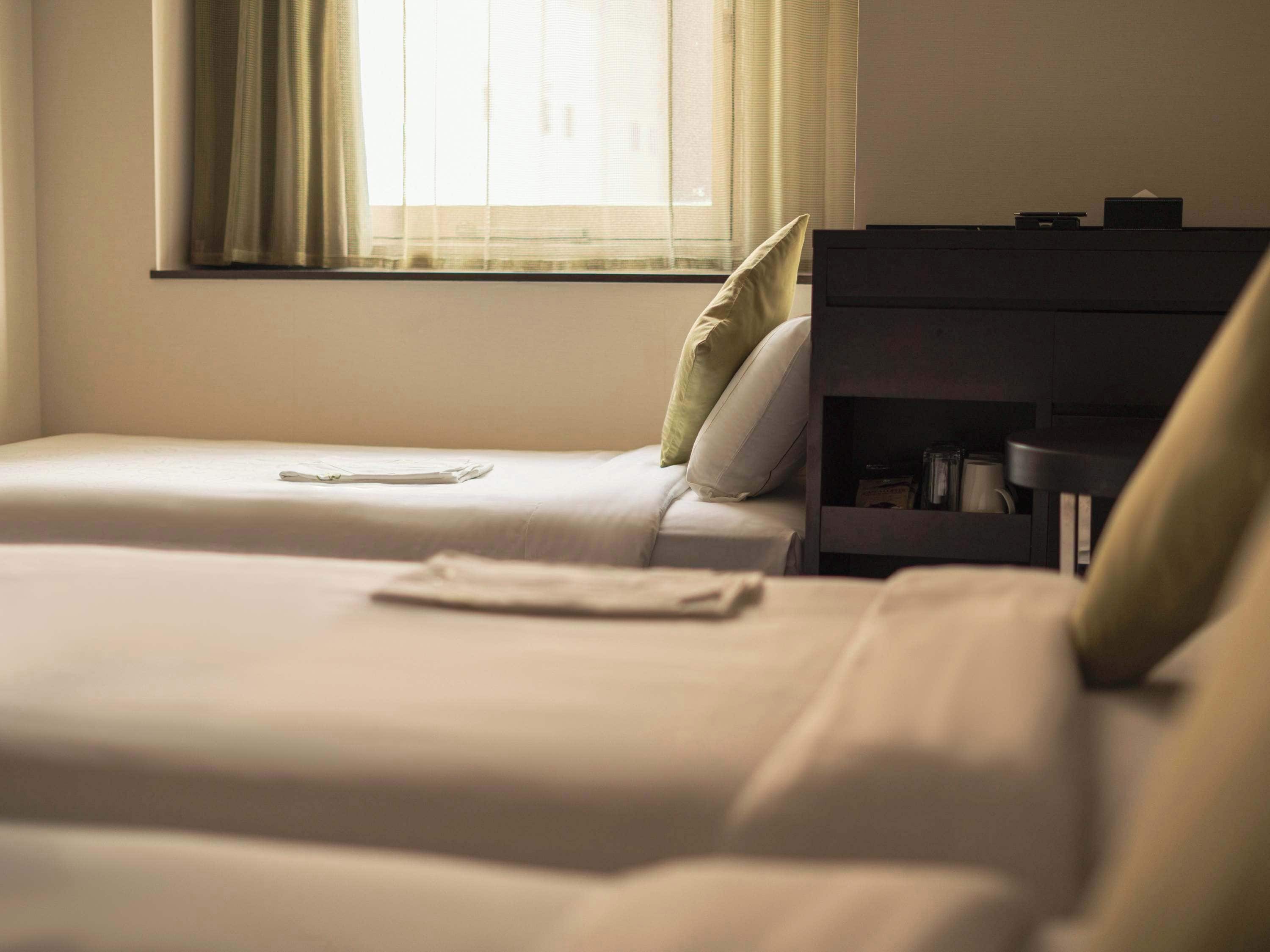 A room with two beds, a nightstand, and a window with curtains.