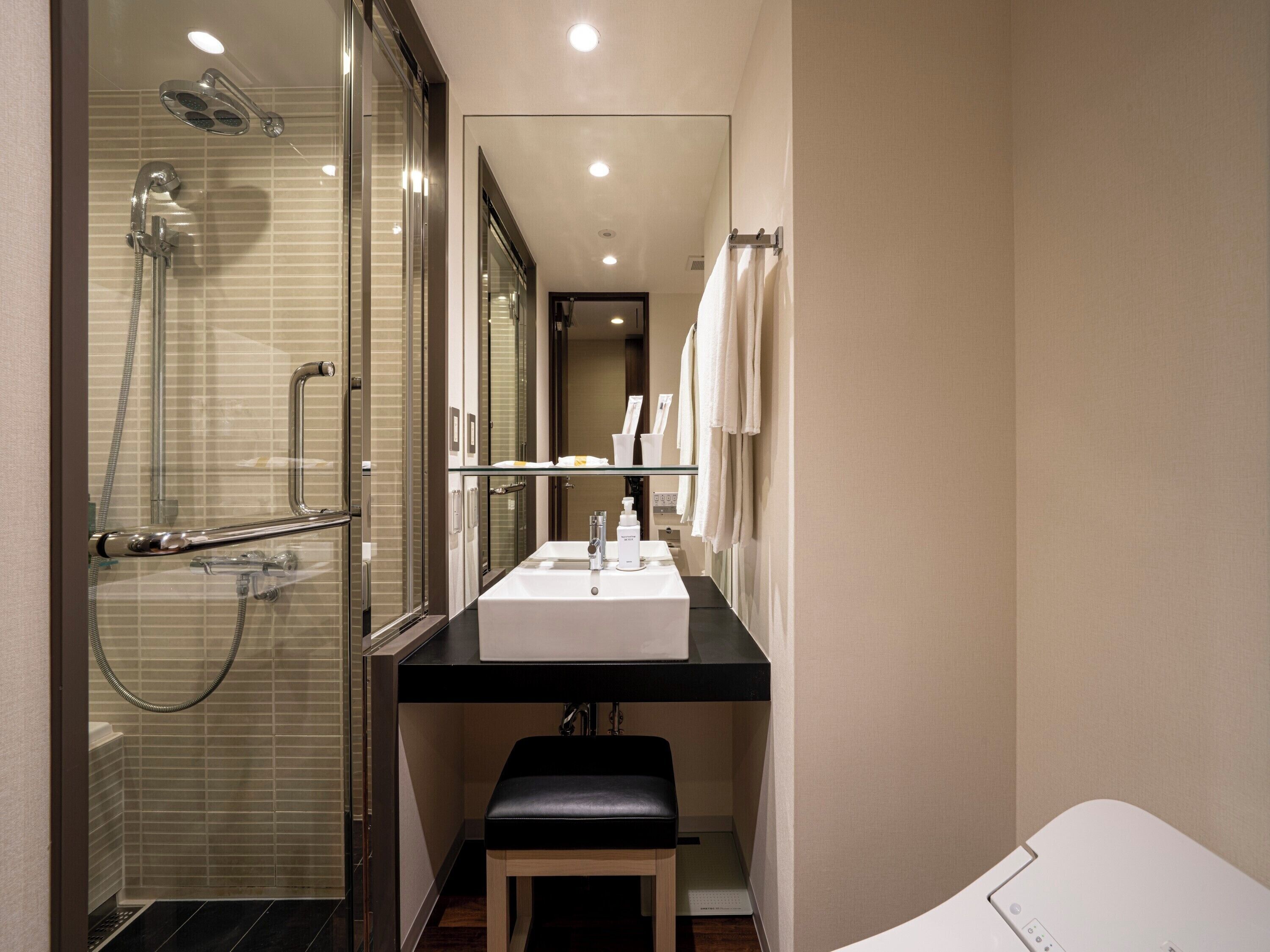 Une salle de bain moderne avec une douche à parois de verre, un lavabo blanc et un banc.