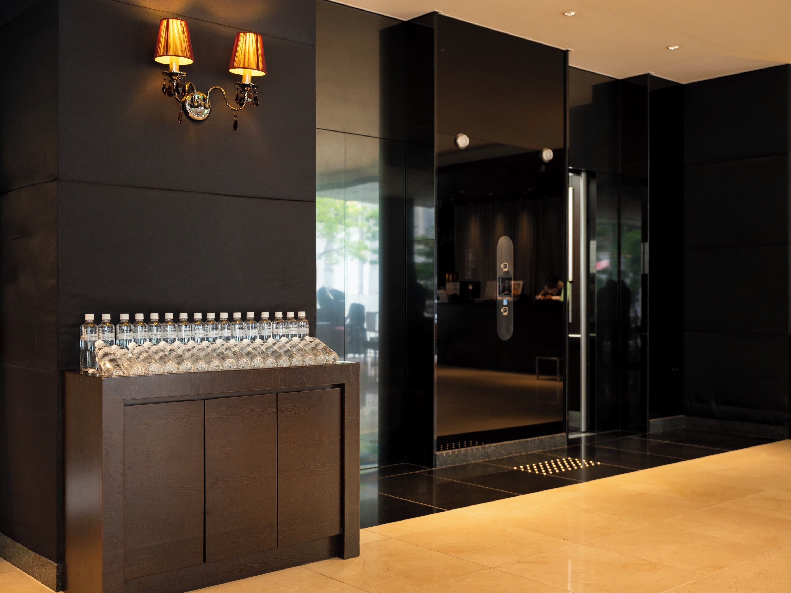 A modern lobby with a water dispenser, wall sconces, and a glass elevator.