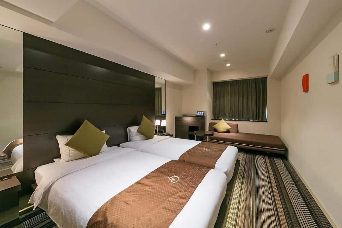 Een hotelkamer met twee bedden, een bank, een televisie en een raam.