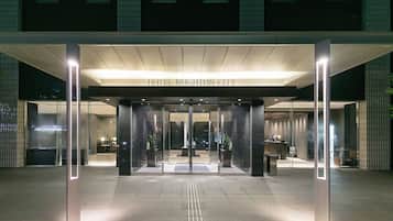 A hotel entrance with a modern design, featuring a glass facade, a reception desk, and a clear pathway leading to the entrance.
