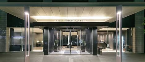 A hotel entrance with a modern design, featuring a glass facade, a reception desk, and a clear pathway leading to the entrance.