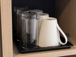 Un plateau sur lequel se trouvent une bouteille en verre transparent et une tasse blanche, le tout posé sur une étagère en bois.