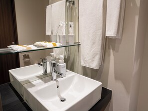 Een badkamer met twee wastafels, een glazen plank met toiletartikelen, en handdoeken aan de muur.