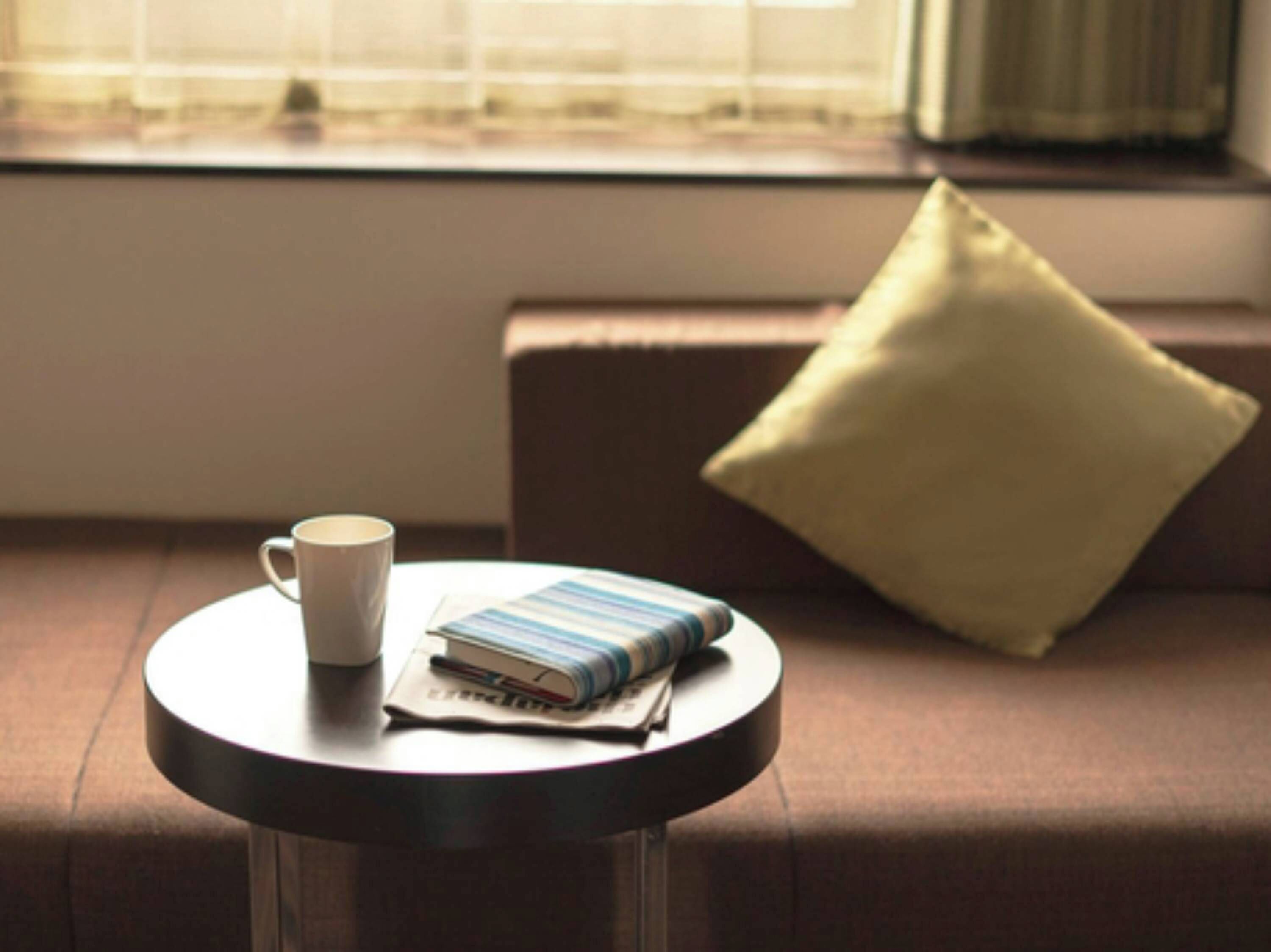 A round table with a white mug and a stack of magazines.