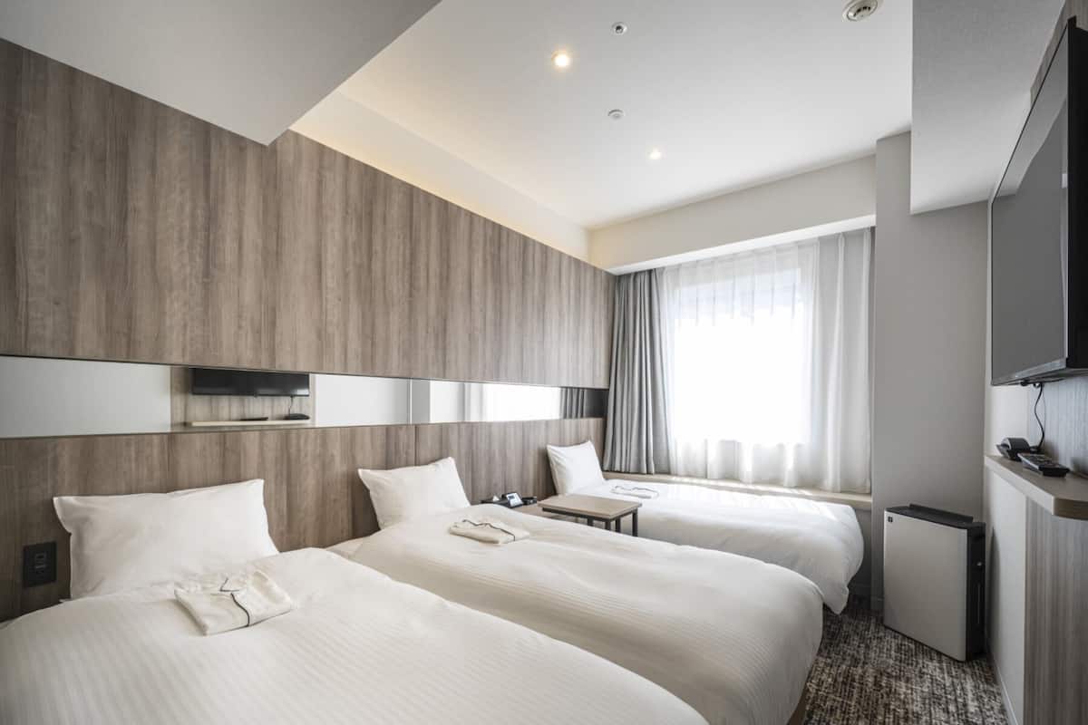 Een hotelkamer met twee bedden, een televisie, een bureau en een klein keukenblok.