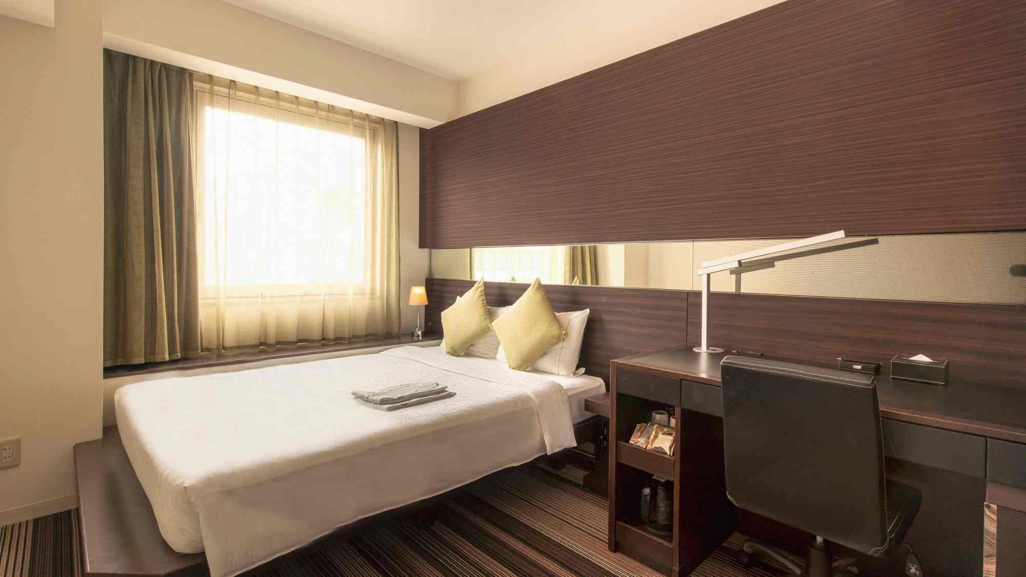 A hotel room with a bed, bedside table, lamp, and a large window with curtains.