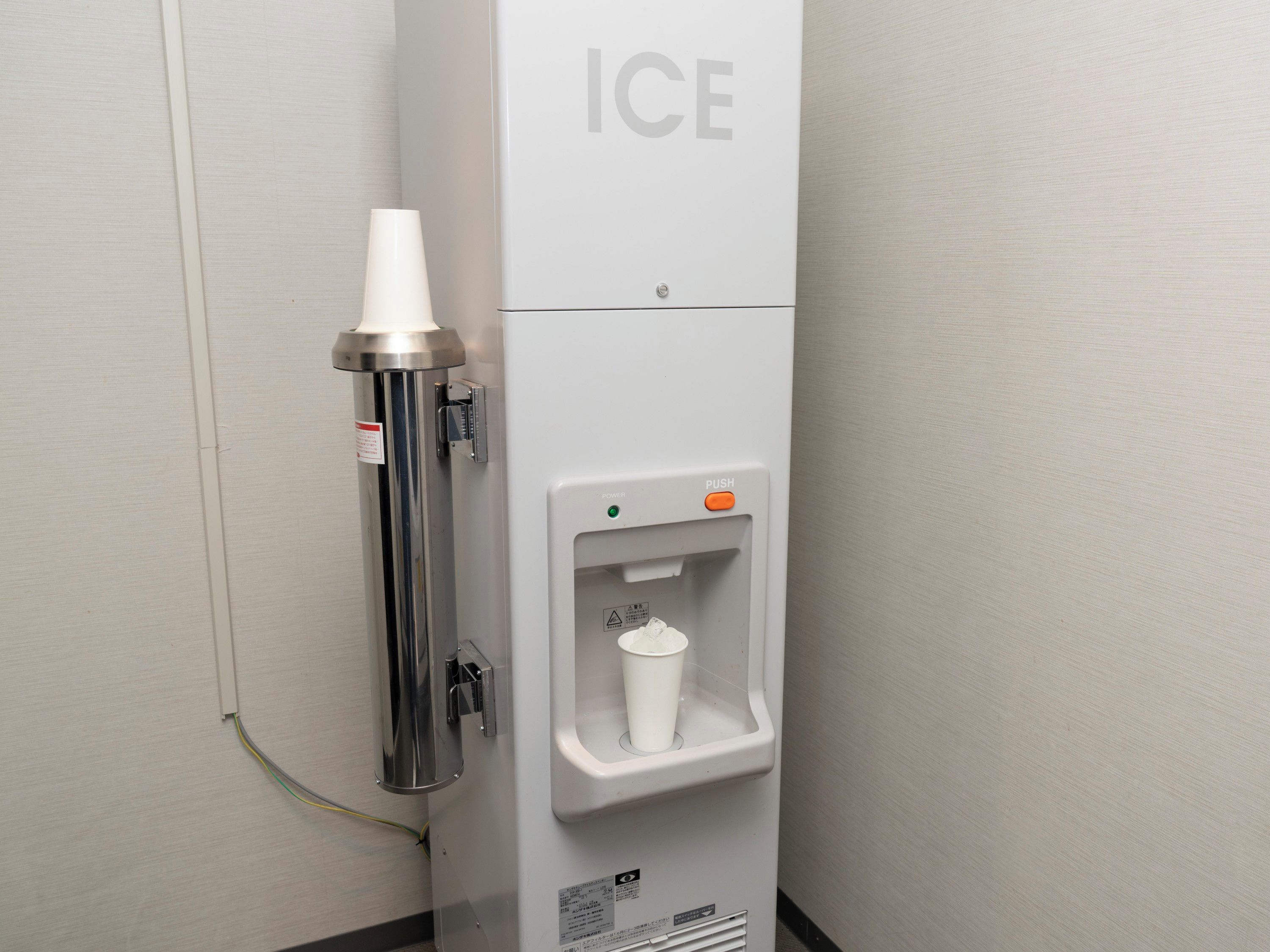 A water dispenser with a cup holder, labeled 'ICE,' and a push button for operation.