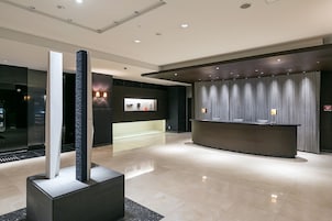 Una hall moderna con una reception, un'imponente colonna e un lampadario a parete.