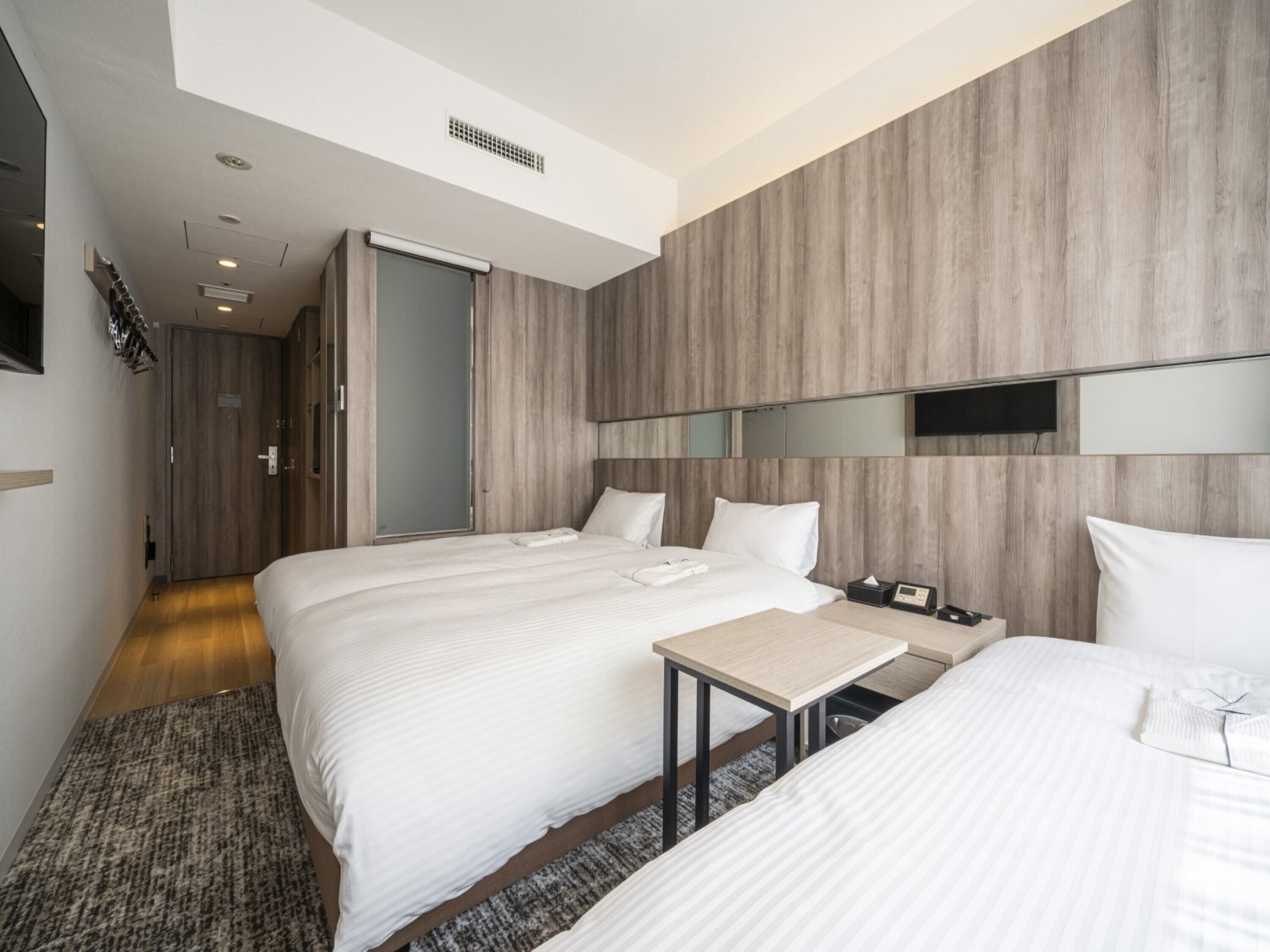 Une chambre d’hôtel moderne équipée de deux lits, d’une petite table, d’une table de chevet, d’une télévision et d’une armoire.