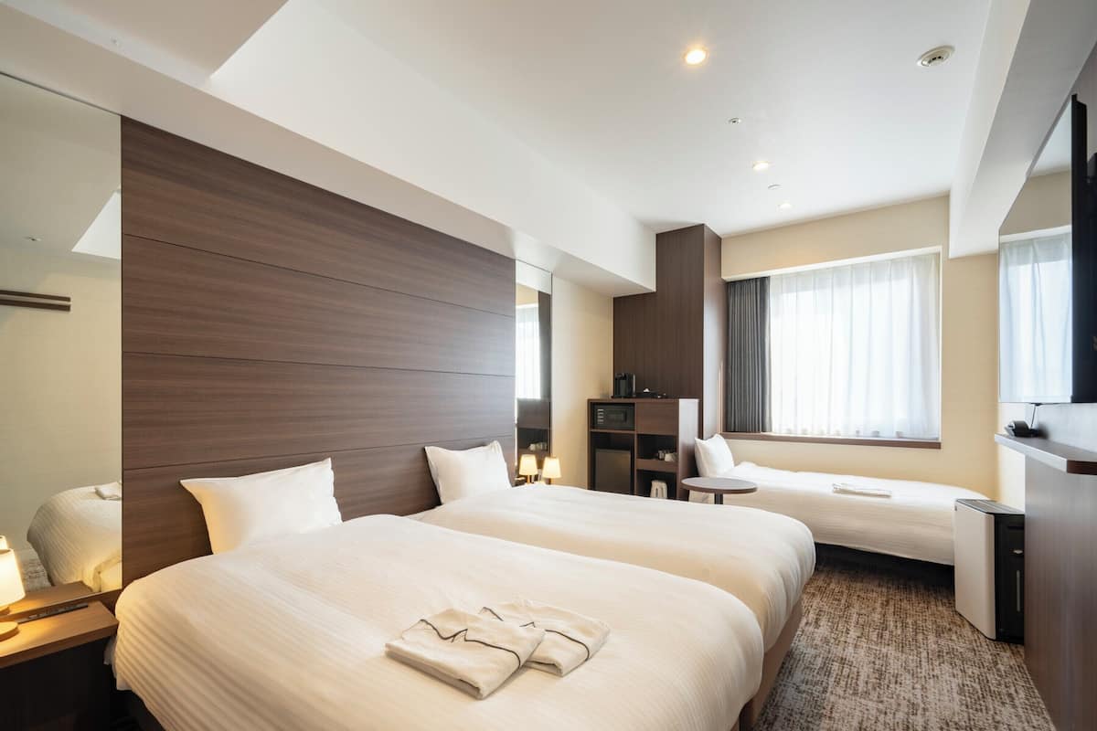 Een hotelkamer met twee bedden, een bureau, een stoel, een televisie en een raam met gordijnen.