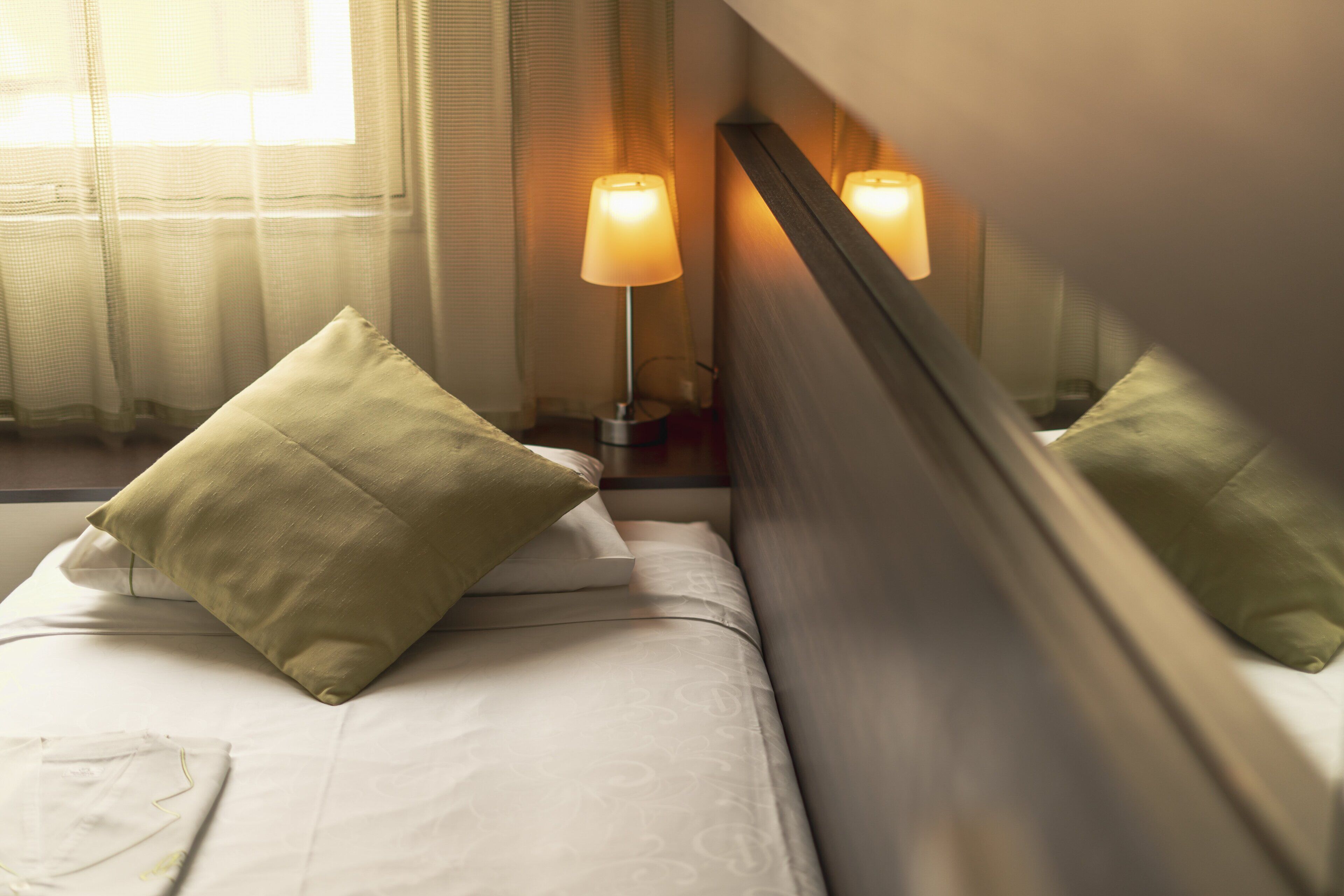 Ein Hotelzimmer mit Bett, Kissen, Nachttisch, Lampe und Spiegel.