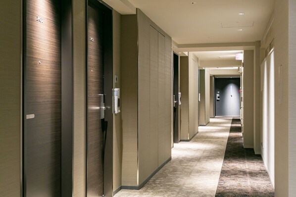 A hotel corridor with multiple doors, some with numbers, and a carpeted floor.