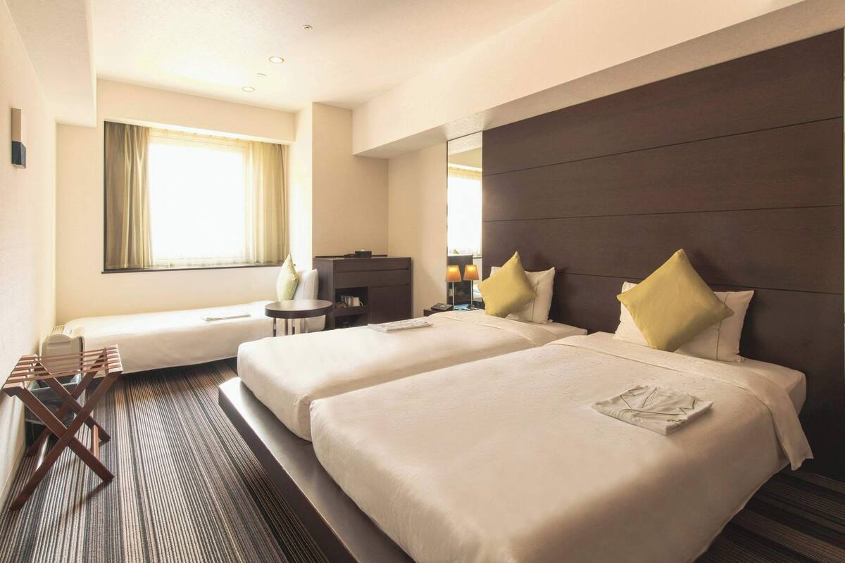 Een hotelkamer met twee bedden, een bureau, een stoel, een kleine tafel en een raam met gordijnen.