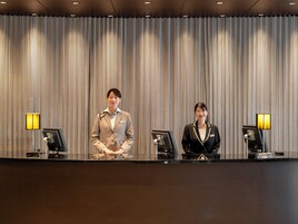 Two receptionists standing behind a reception desk with a striped curtain backdrop and desk lamps.