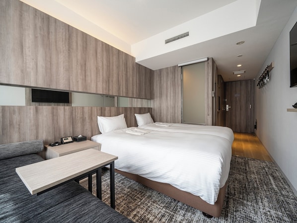 Une chambre d’hôtel moderne équipée d’un grand lit, d’un bureau, d’un canapé et d’un téléviseur à écran plat fixé au mur.