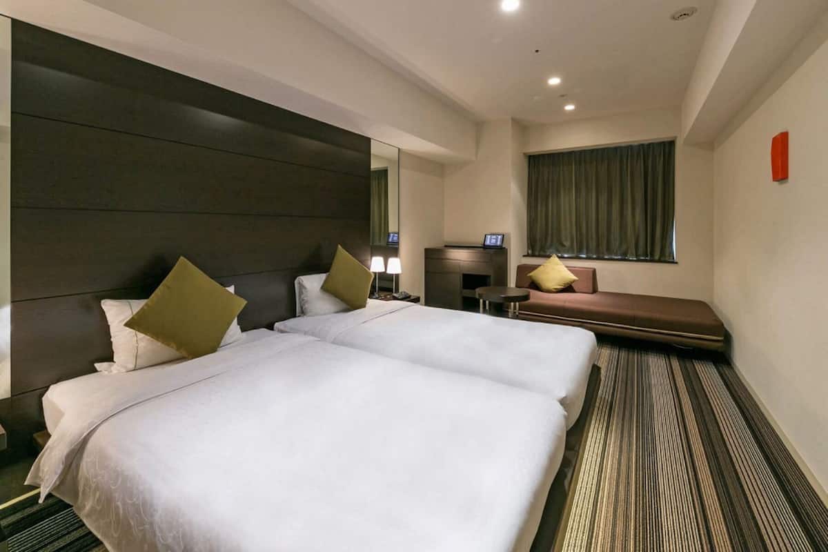 Een hotelkamer met twee bedden, een bank, een televisie en een tafeltje.