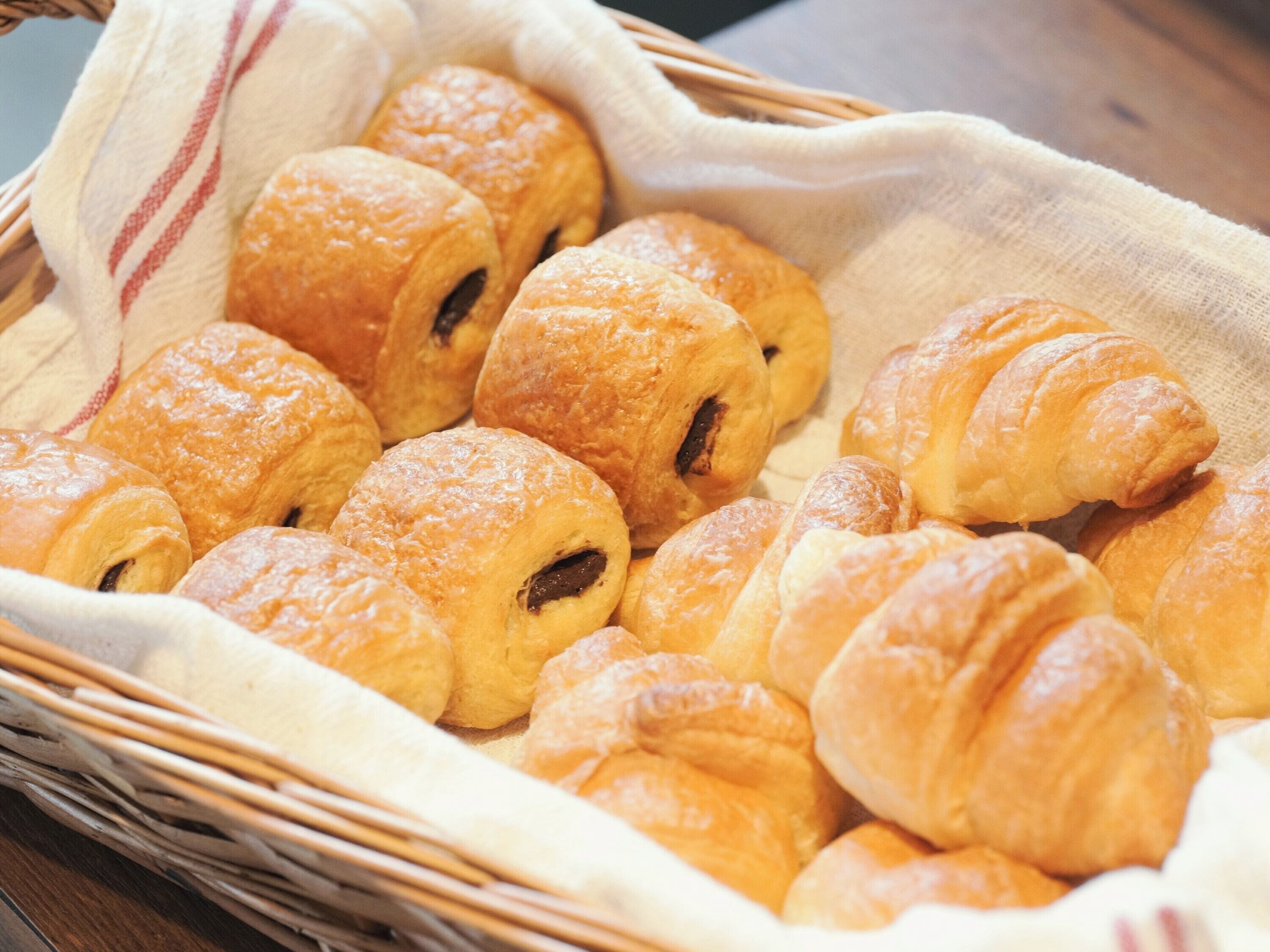 A basket of assorted pastries, including croissants and chocolate-filled items, placed on a cloth.