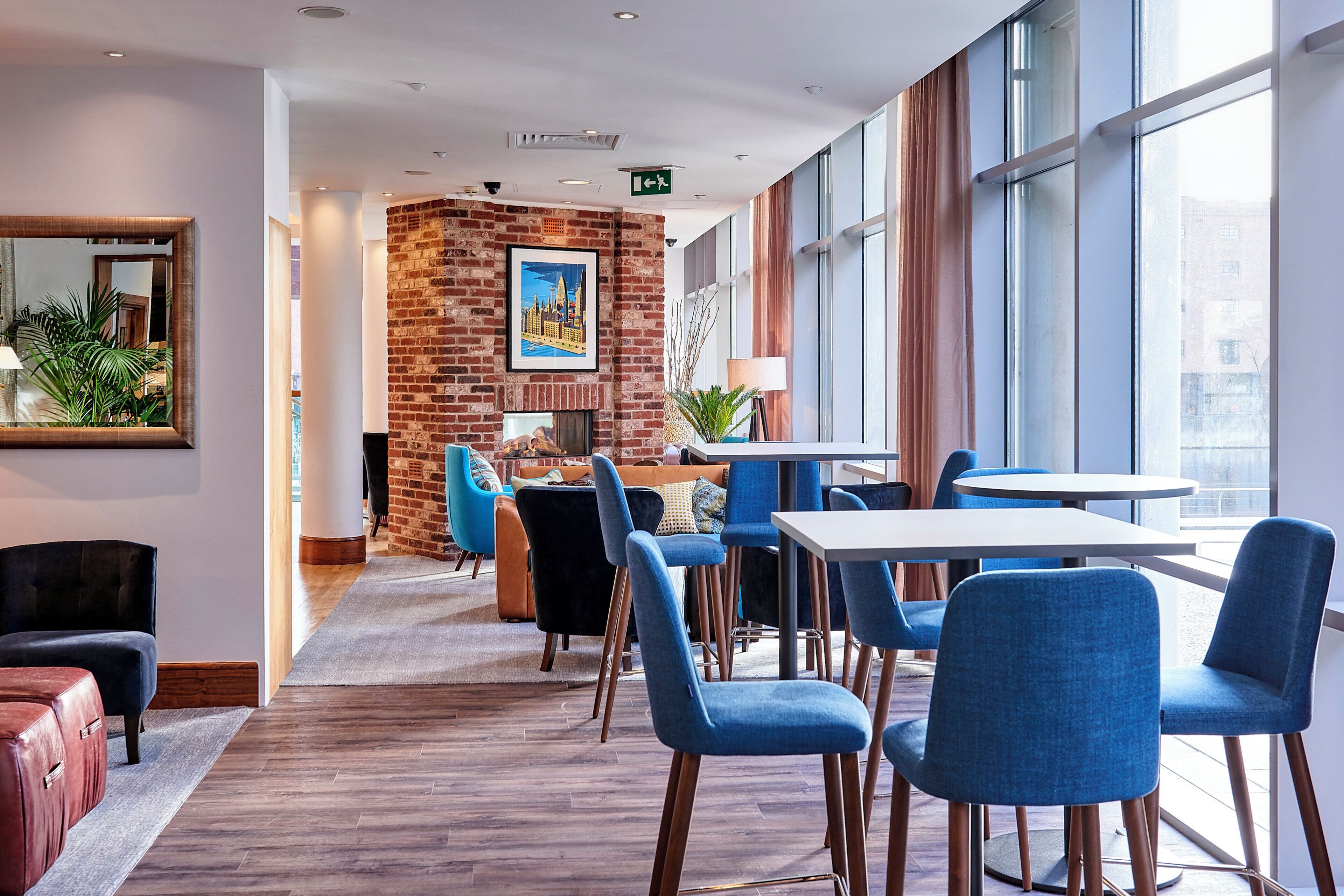 A modern hotel lobby with a brick wall, a fireplace, and a seating area with blue chairs and a white table.
