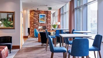 A modern hotel lobby with a brick wall, a fireplace, and a seating area with blue chairs and a white table.