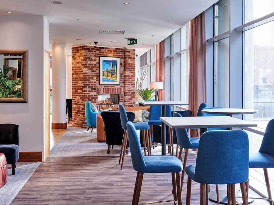 A modern hotel lobby with a brick wall, a fireplace, and a seating area with blue chairs and a white table.
