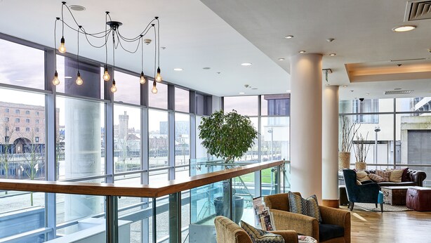A spacious lobby with large windows, a staircase, and modern furniture.