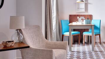 Una habitación moderna con un sillón beige, una mesita con lámpara, una silla azul y una mesa de comedor de madera con sillas.