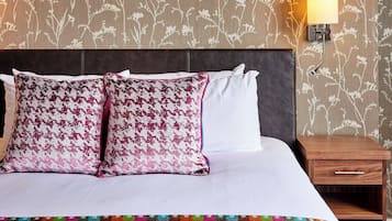 Una cama con dos almohadones estampados, una mesita de noche y una lámpara.