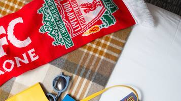 A checkered blanket with a red scarf featuring a white embroidered design, a pair of blue sunglasses, a yellow object, and a blue item with a geometric pattern.