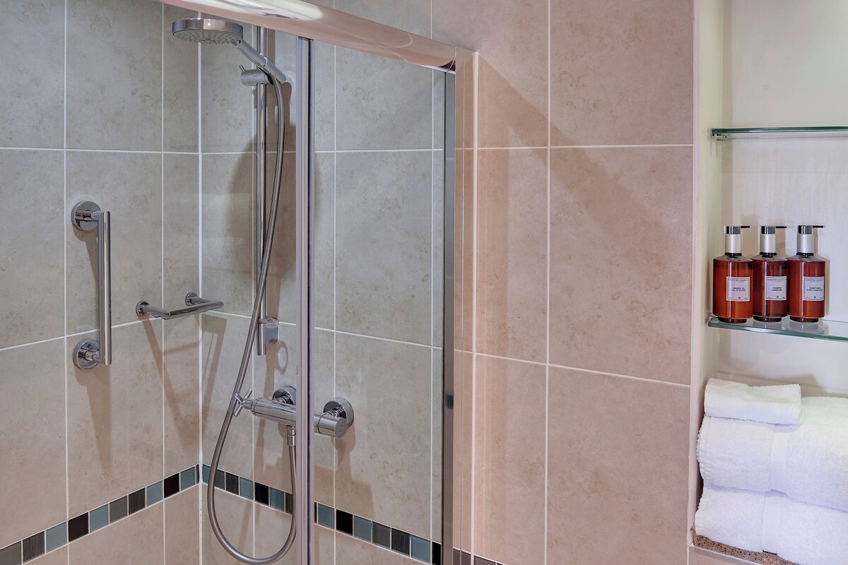 A shower area with a glass door, a towel rack with folded towels, and a shelf with toiletries.