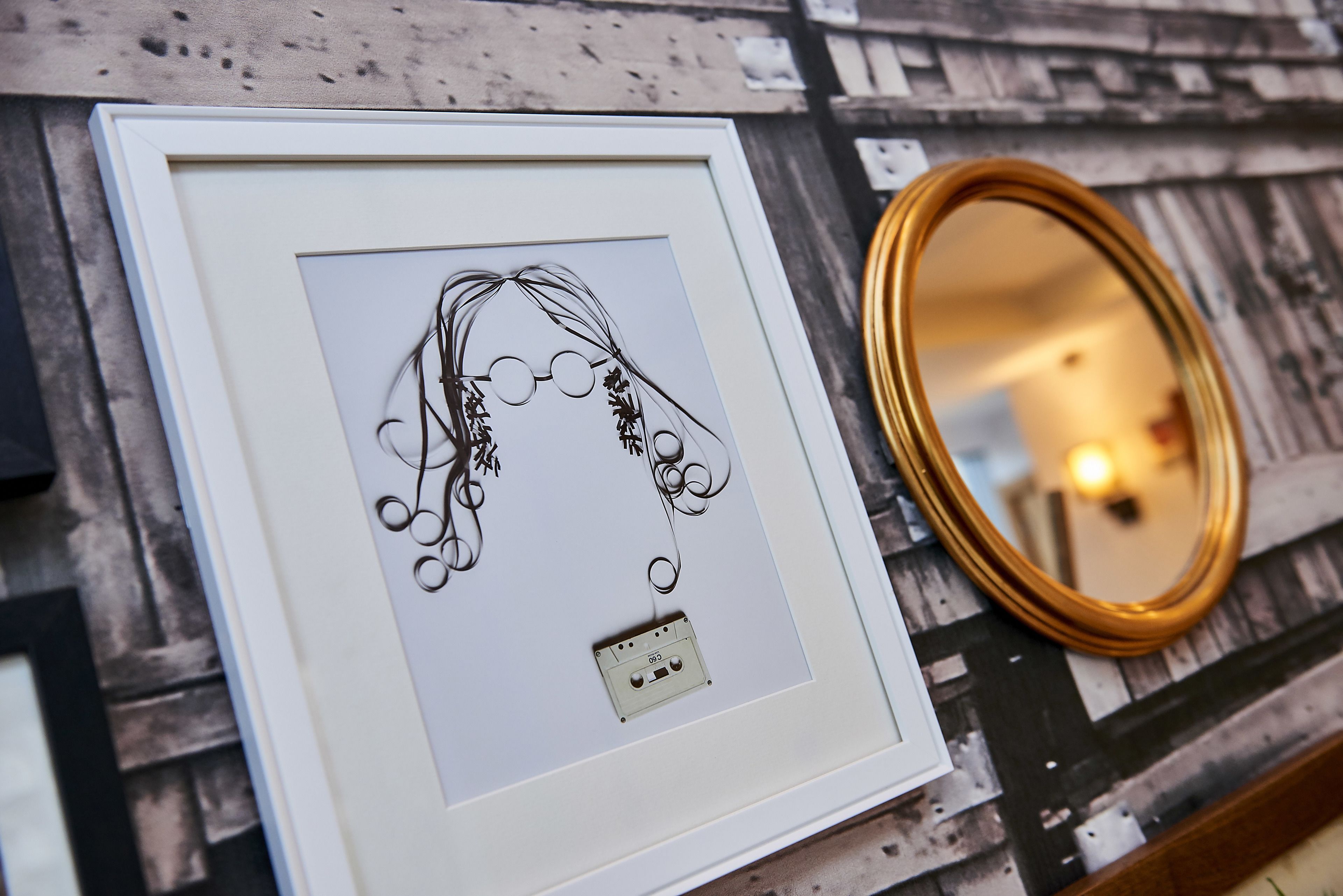 A framed artwork with a cassette tape, a mirror, and a wooden surface.