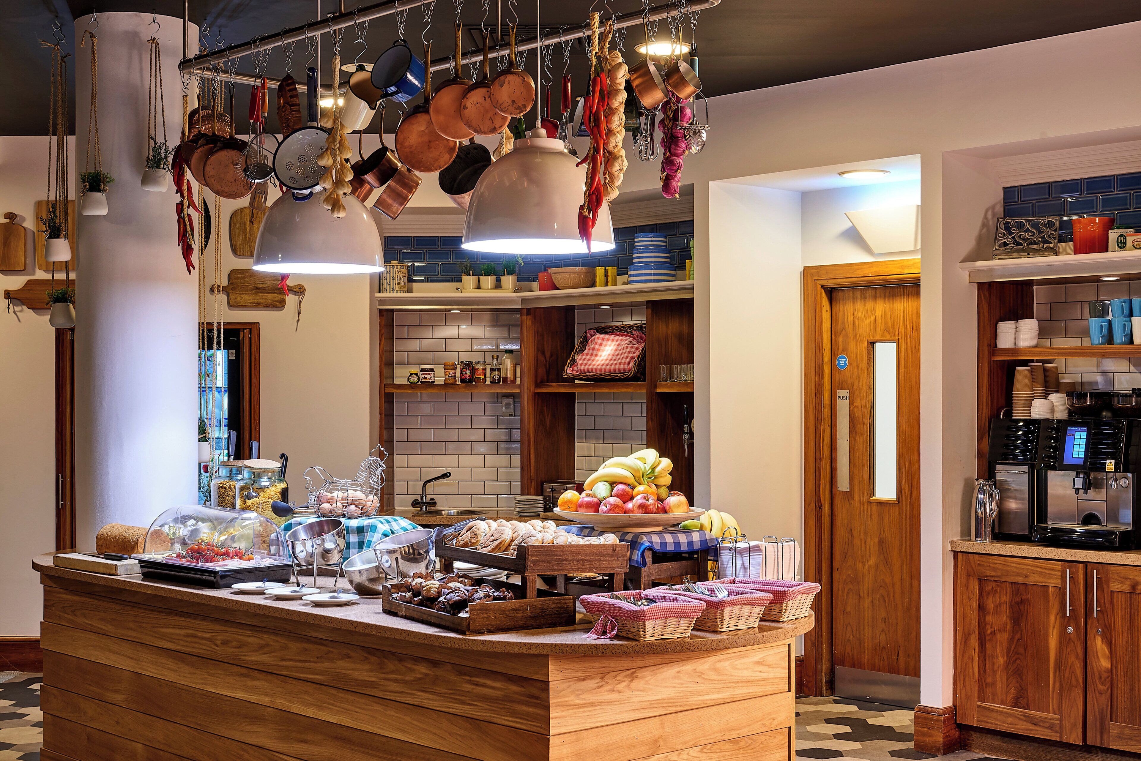 A kitchen area with hanging pots, a fruit display, and a coffee machine.