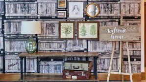 A rustic wall with wooden crates, framed artwork, a lamp, and vintage suitcases.