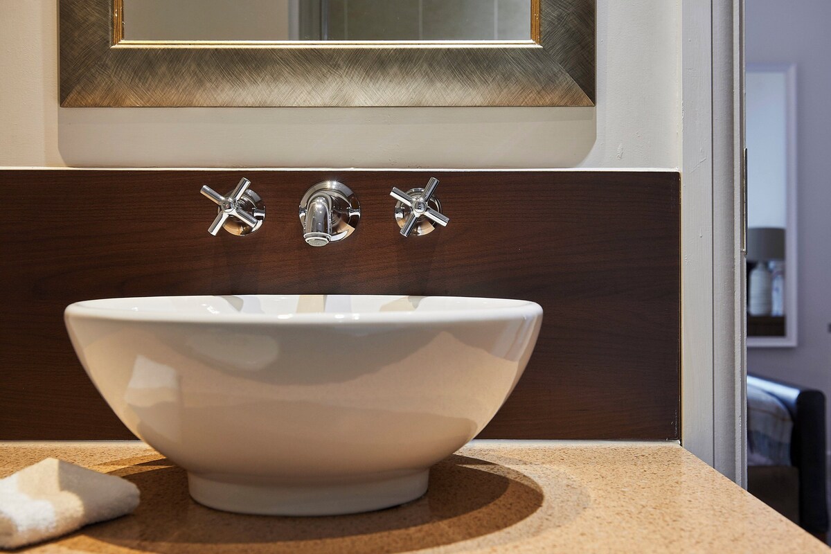 A white basin with a chrome faucet, mounted on a brown countertop with a wooden panel above.