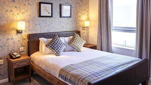 A neatly made bed with a plaid blanket, two bedside lamps, and a nightstand with a phone.