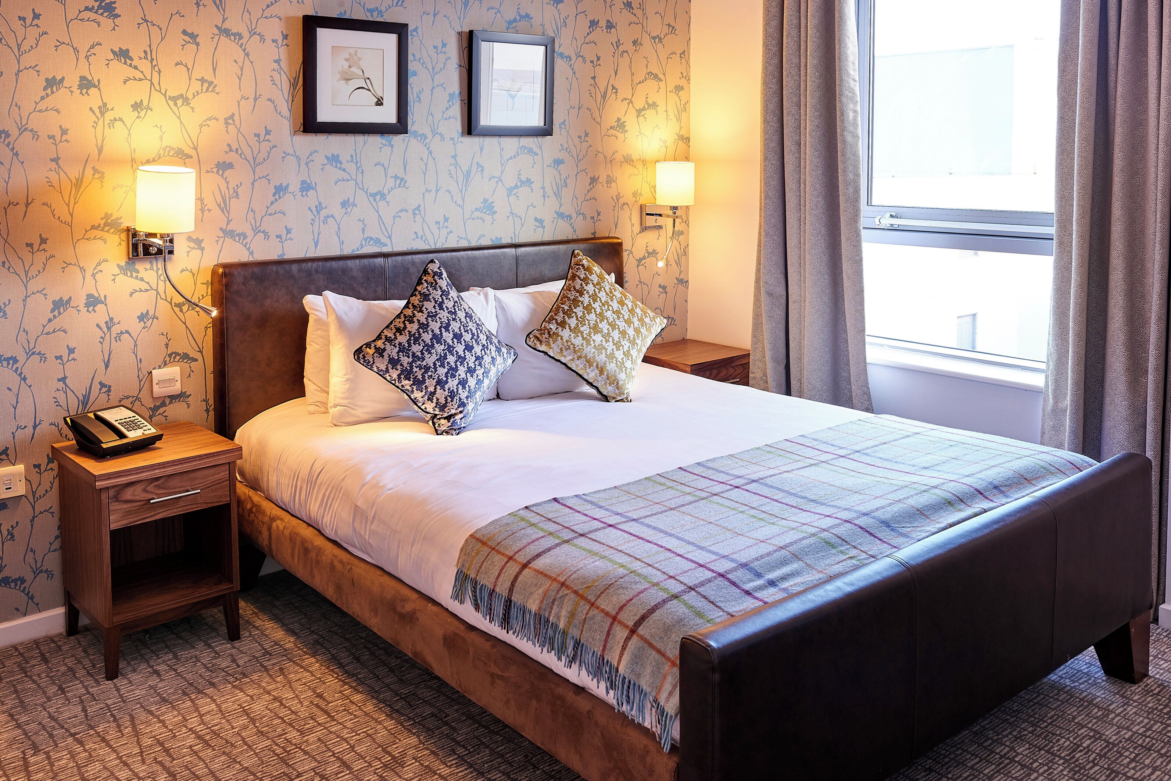 A hotel room with a large bed, two bedside tables, a telephone, and a window with curtains.