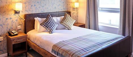 A hotel room with a large bed, two bedside tables, a telephone, and a window with curtains.