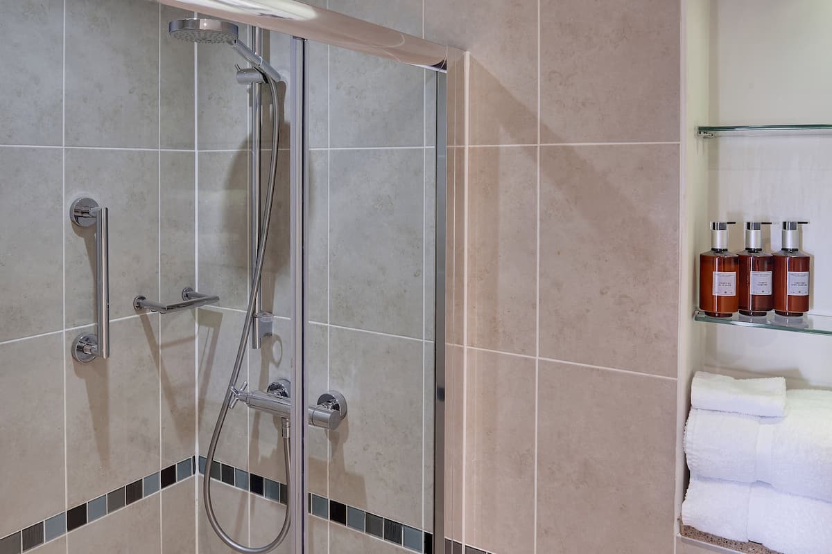Un espacio de ducha con puerta de vidrio, un perchero con toallas dobladas y un estante con artículos de aseo.