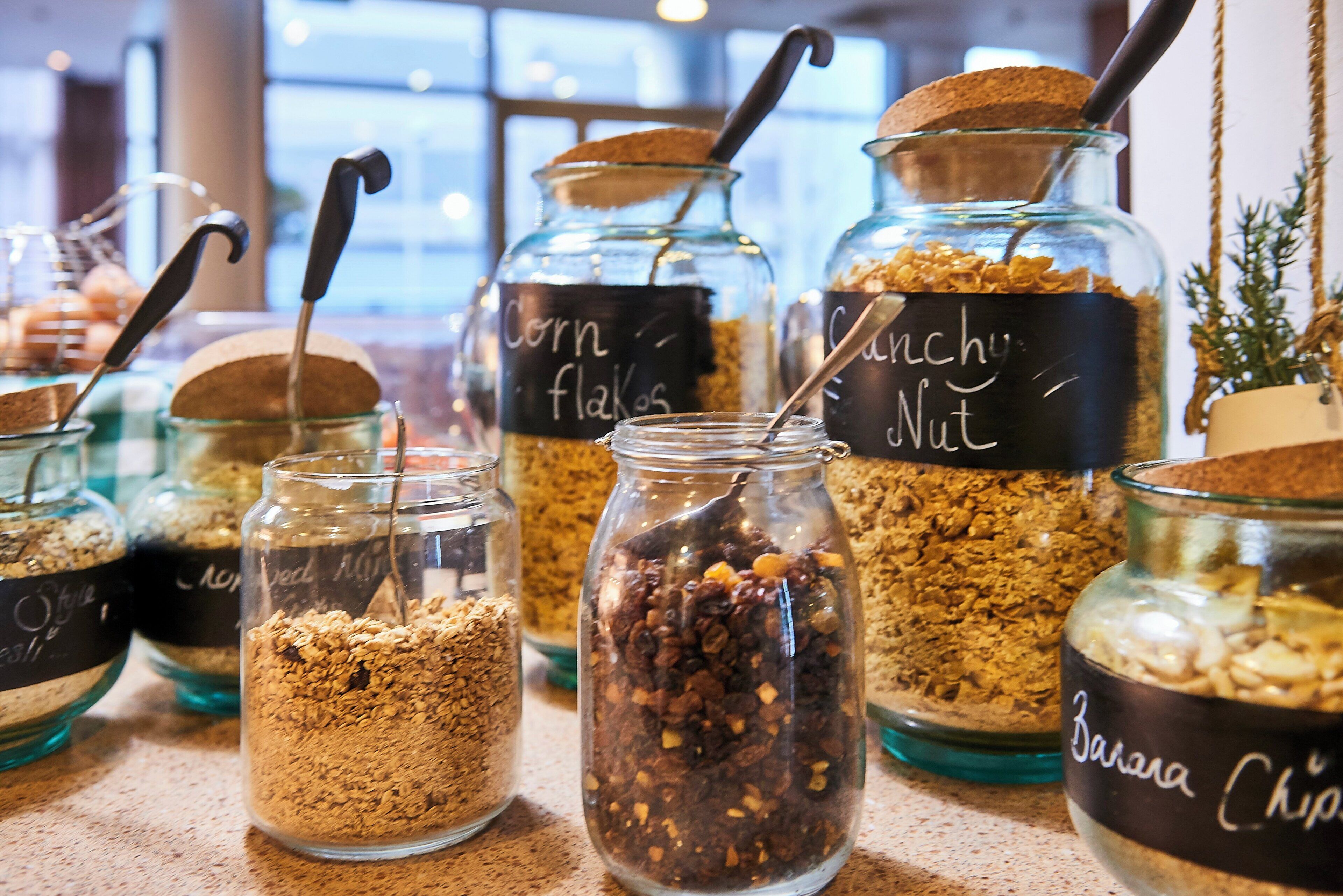 Glass jars with labels containing different food items like corn flakes, granola, and nuts.