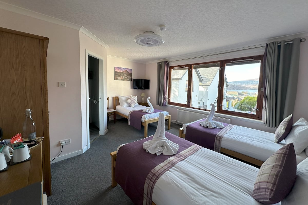 A hotel room with two beds, a desk, a chair, a television, and a window with a view.