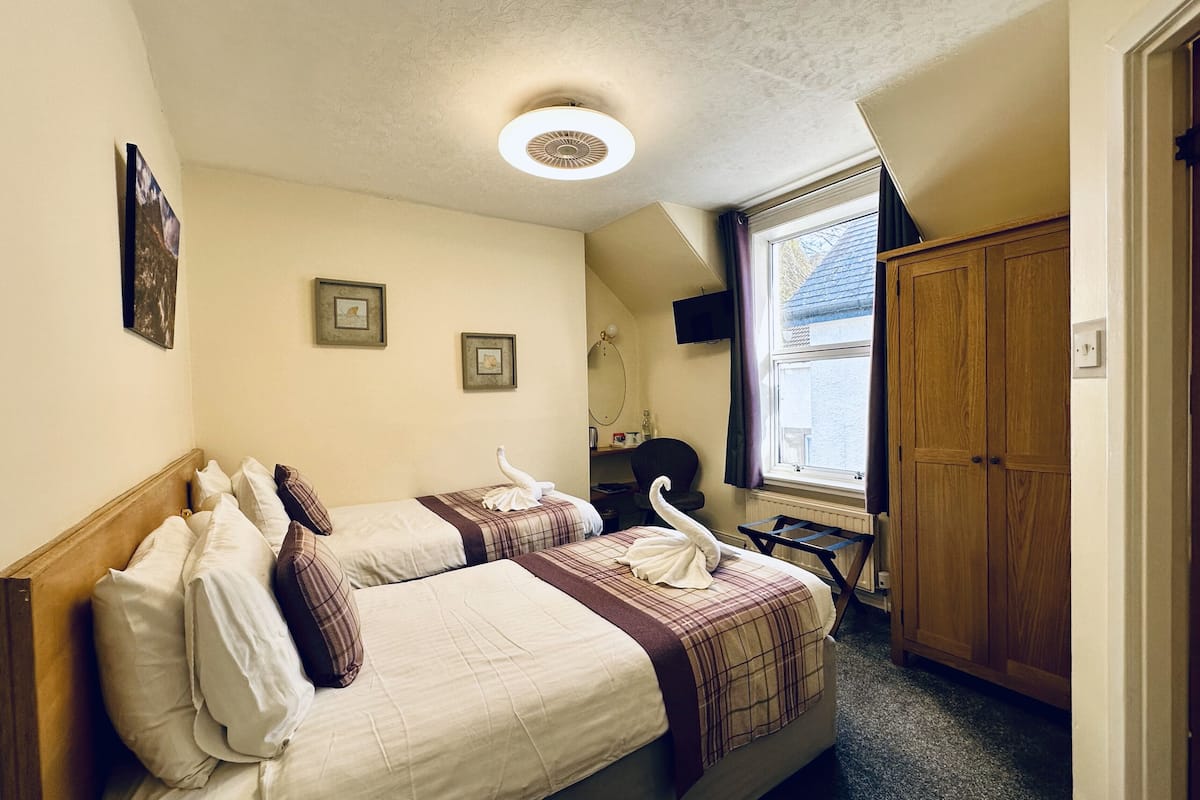 A bedroom with two beds, a wooden wardrobe, a window with curtains, and a ceiling light.