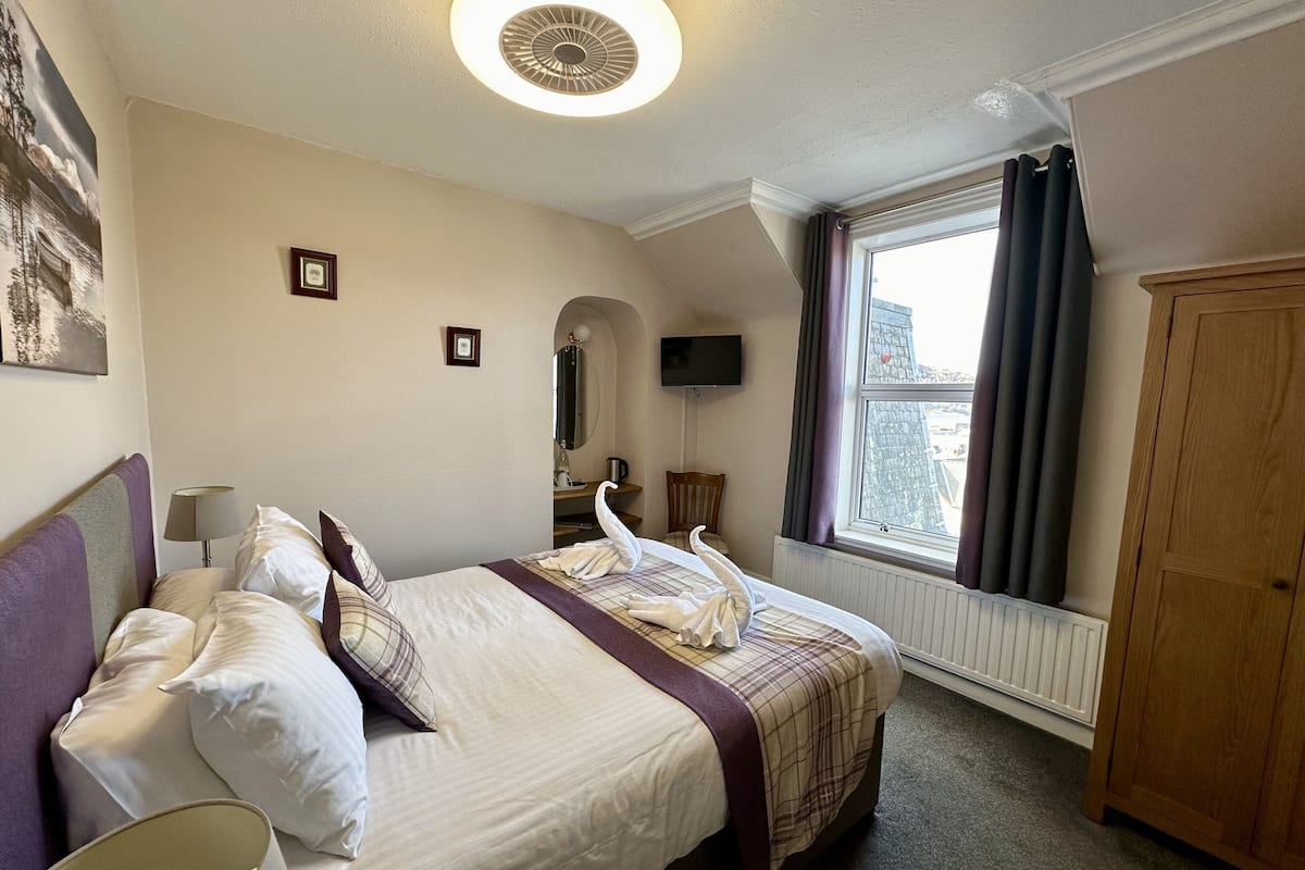 A hotel room with a bed, a television, a window with curtains, and a wooden wardrobe.