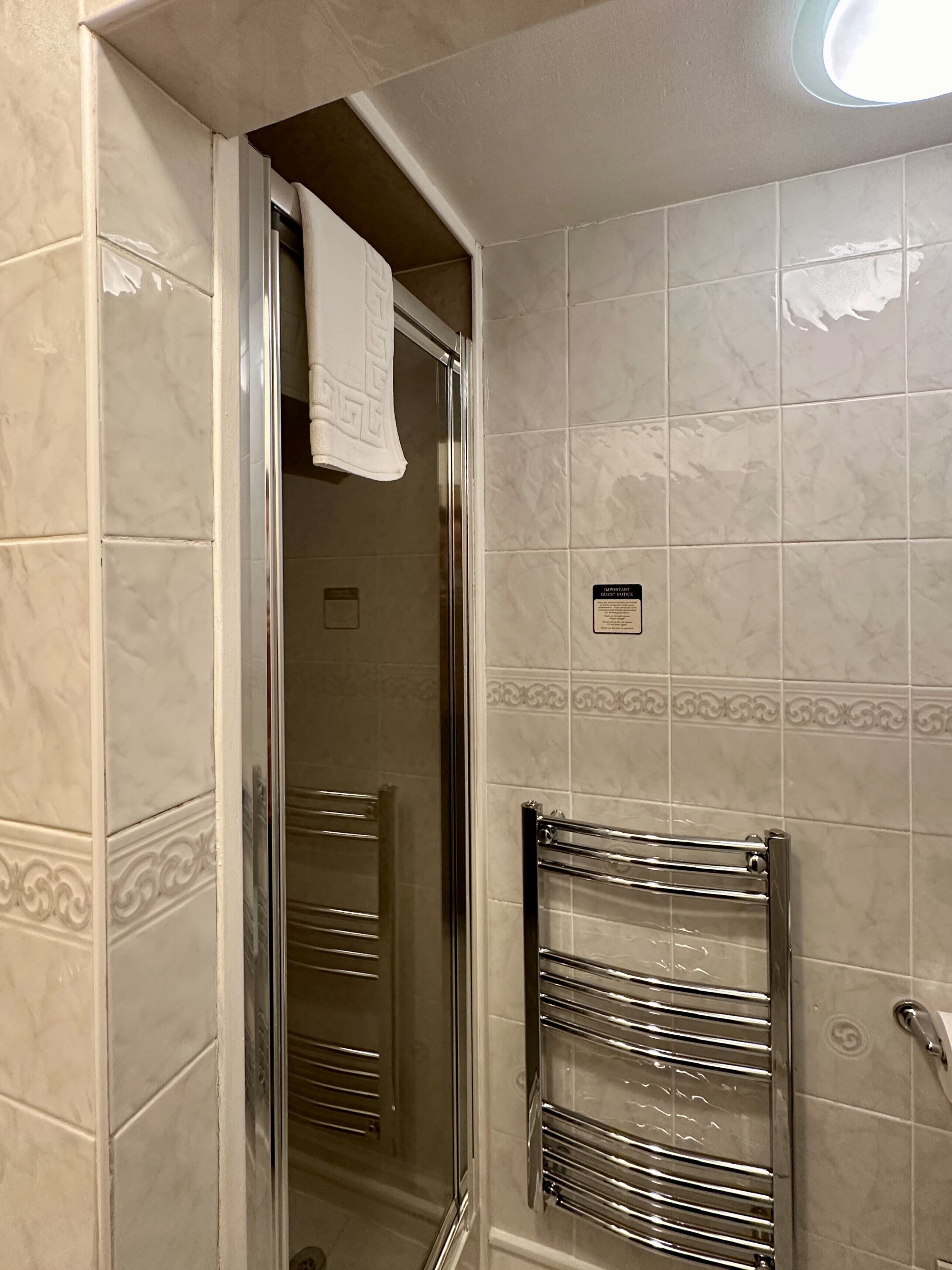 A bathroom with a glass shower door, a towel hanging on the door, and a chrome towel rack.