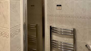 A bathroom with a glass shower door, a towel hanging on the door, and a chrome towel rack.