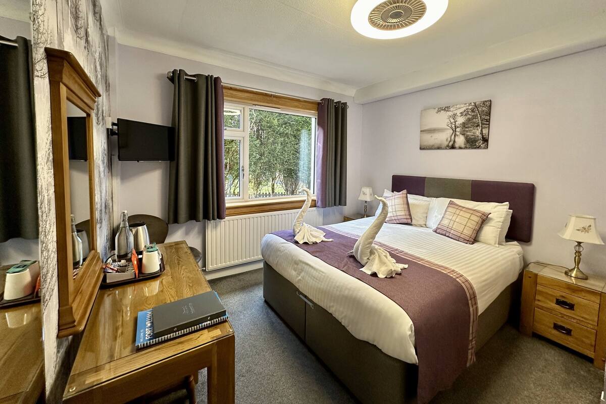A hotel room with a bed, bedside table, lamp, and a window with curtains.