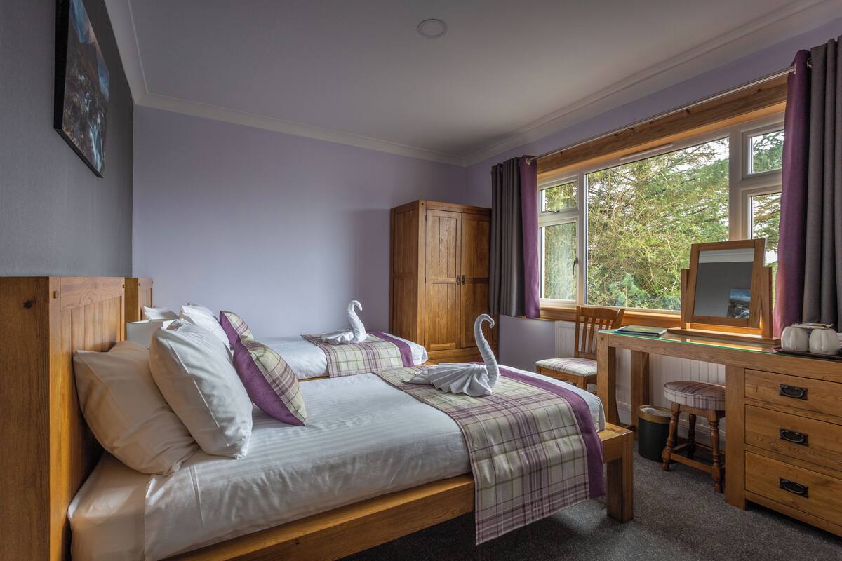 A bedroom with a bed, wooden wardrobe, desk, chair, and a window with curtains.