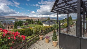 Un balcón con pérgola, plantas en macetas y vistas a una zona residencial con casas y colinas.