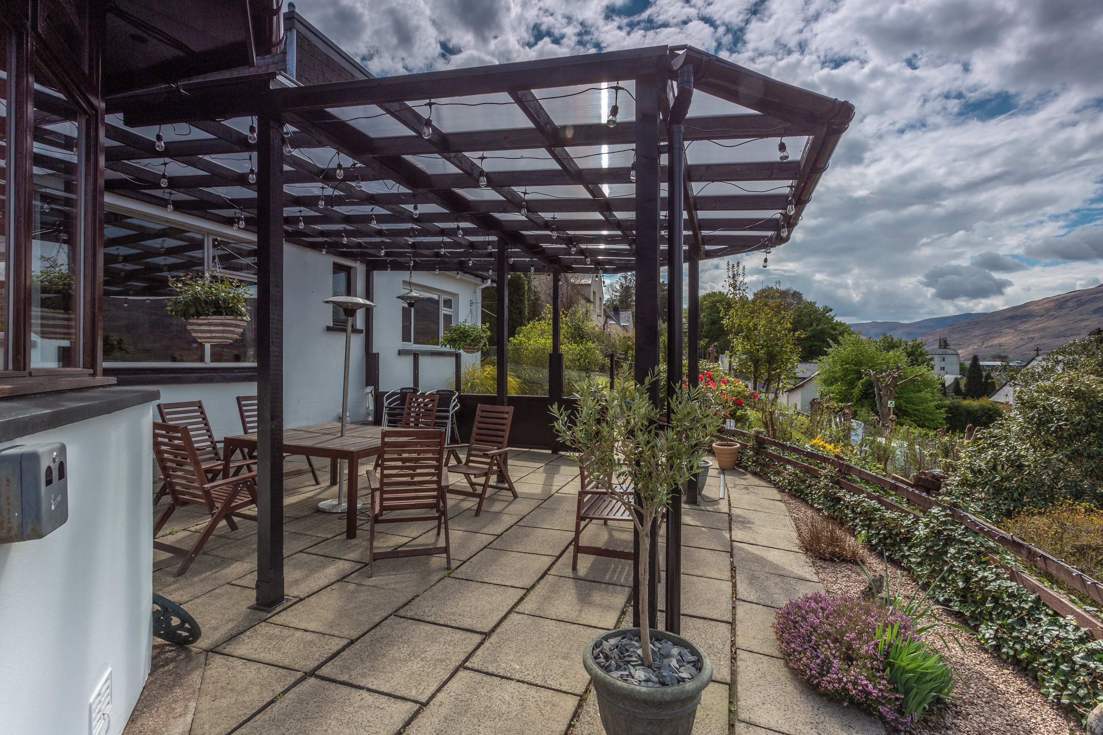 A covered patio with outdoor furniture, a pergola, and a garden area with various plants.
