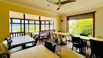 A dining area with tables and chairs, large windows with a view, and a ceiling fan.